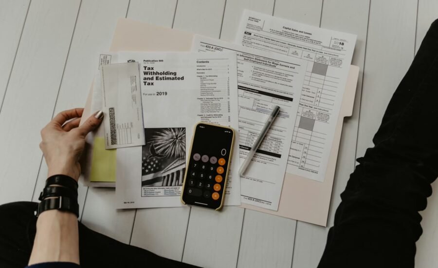 Calculator, financial documents and pen on a desk beside a laptop in a professional office setting