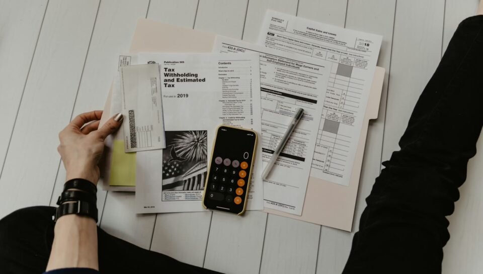 Calculator, financial documents and pen on a desk beside a laptop in a professional office setting